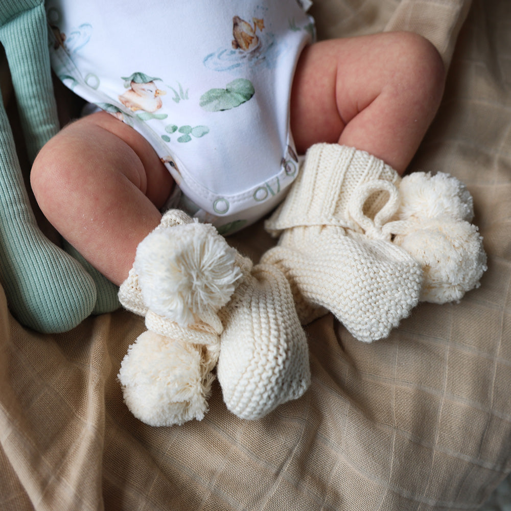 Soft cream organic cotton knit baby booties designed to keep newborn feet warm and comfortable, featuring a timeless neutral colour perfect for everyday wear or gifting.